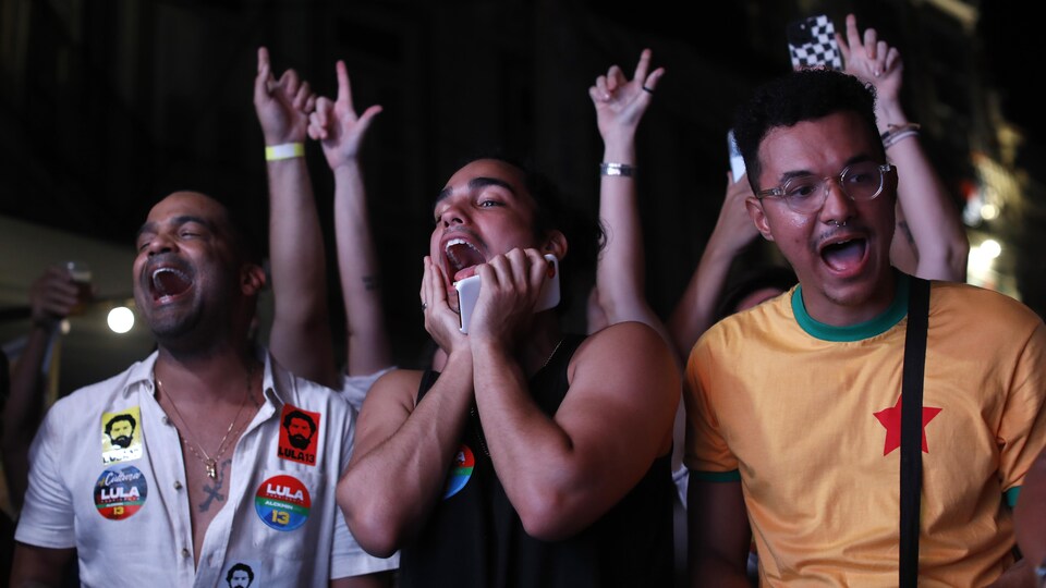 Trois jeunes hommes, arborant des écussons aux couleurs de Lula, crient de joie.