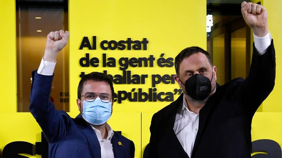 Deux hommes, dont un portant des lunettes, posent le visage couvert d'un masque, le poing levé en signe de victoire.