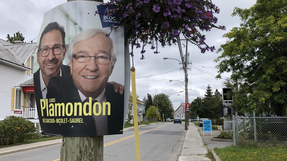 Sur une rue, on aperçoit une pancarte électorale accrochée à un arbre et sur laquelle on voit les visages de Louis Plamondon et de son chef au Bloc québécois Yves-François Blanchet.
