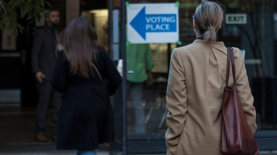 Des électeurs se dirigent vers un bureau de vote. On les voit de dos.