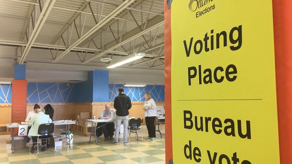 Une affiche, des électeurs et des employés dans un bureau de vote d'Ottawa.