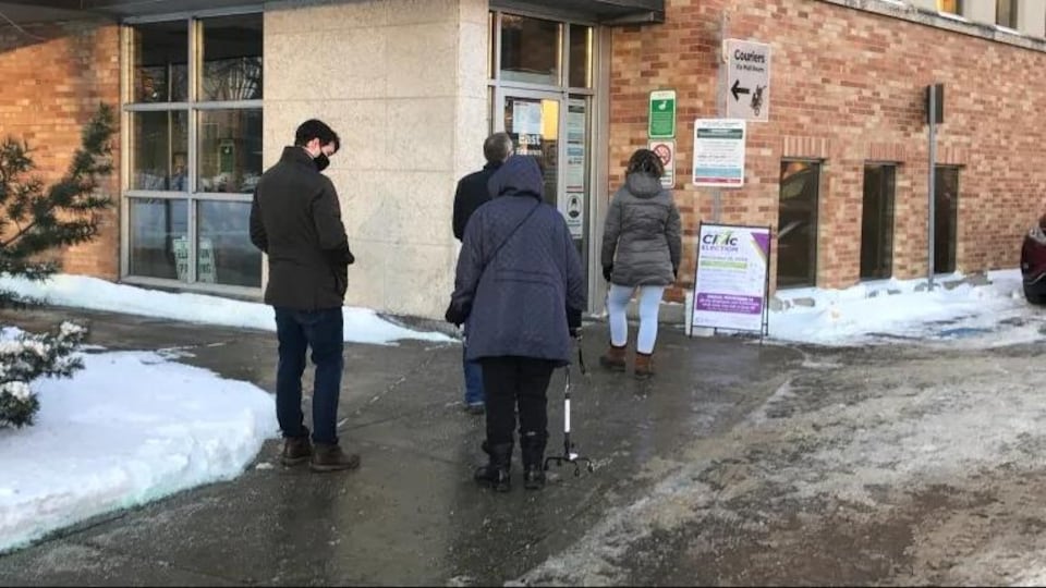 Un petit groupe d'électeurs devant un bureau de vote.