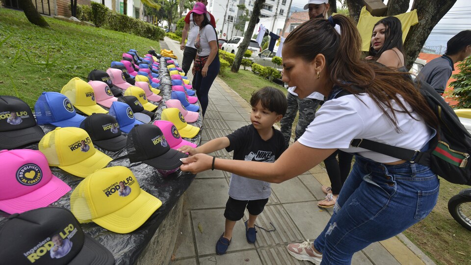 Une femme accompagnée de son jeune fils achète une casquette à l'effigie de Rodolfo Hernandez.