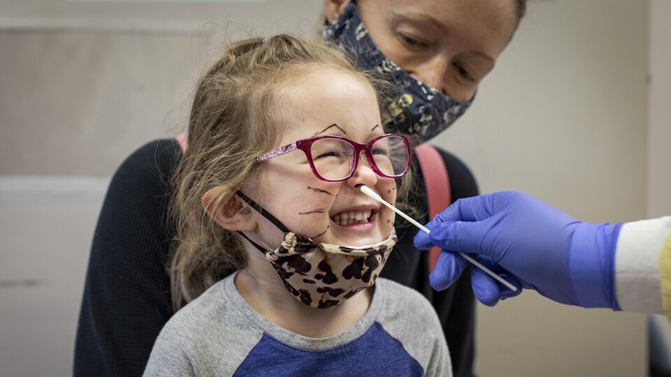 Une fillette se ferme les yeux, alors qu'on lui insère dans le nez une tige de prélèvement pour un test de dépistage.