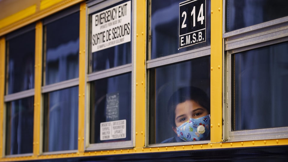 Un élève qui porte un masque regarde par la fenêtre d'un autobus scolaire.
