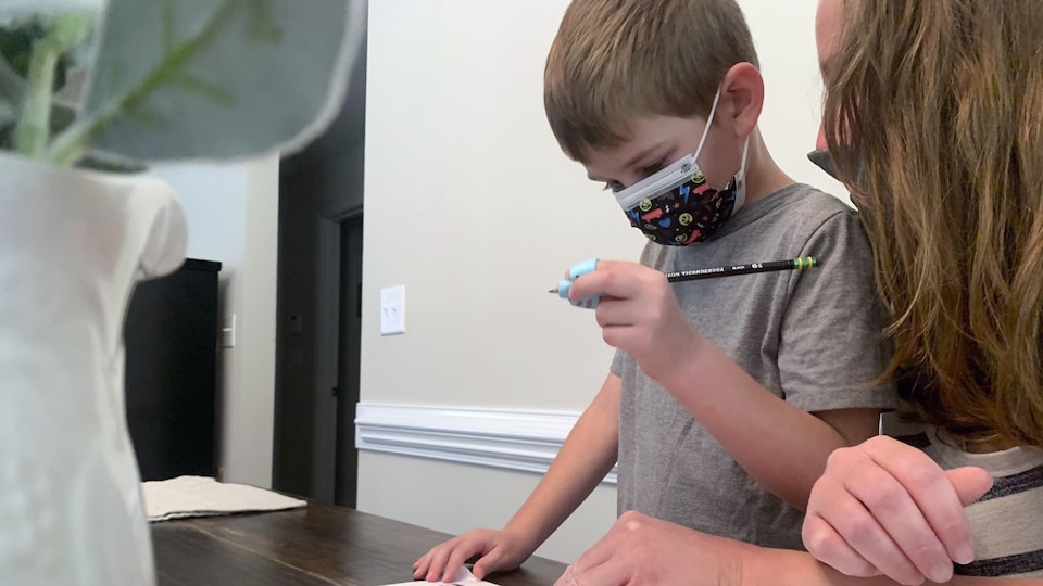 Un enfant qui porte un masque fait ses devoirs avec sa mère.