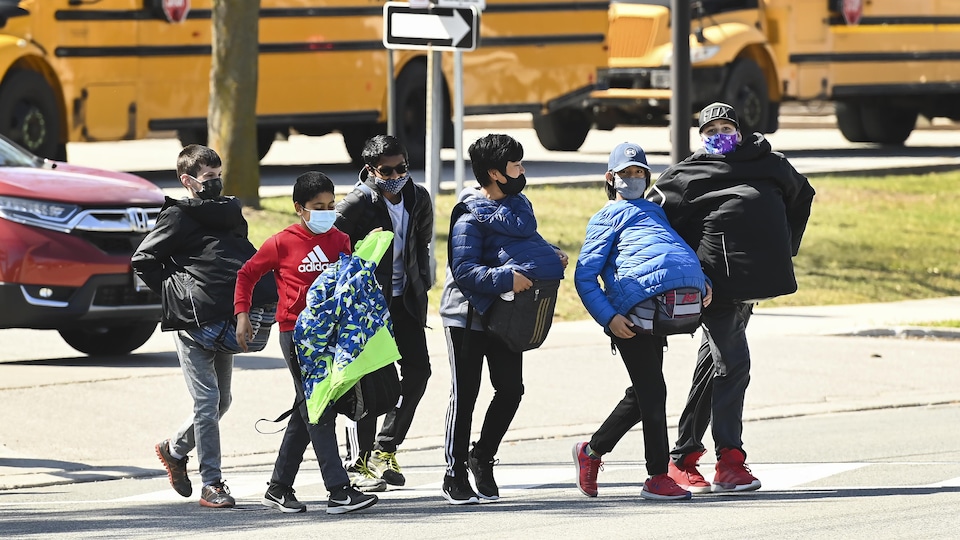 Des élèves qui portent un masque arrivent à l'école en portant leur sac à devant eux.