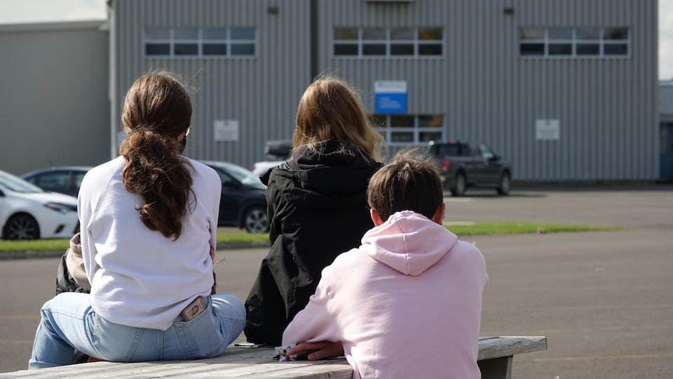 Des élèves sont assis sur une table à pique-nique, devant l'École Antoine-Bernard.
