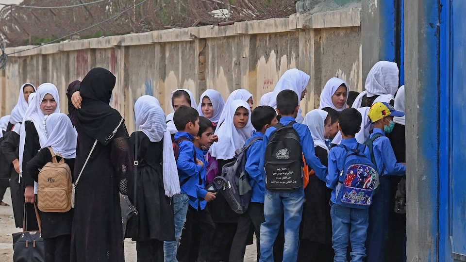 Des garçons et des filles, toutes voilées, devant un bâtiment.