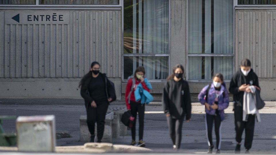 Des élèves portant le masque devant l'entrée d'une école.