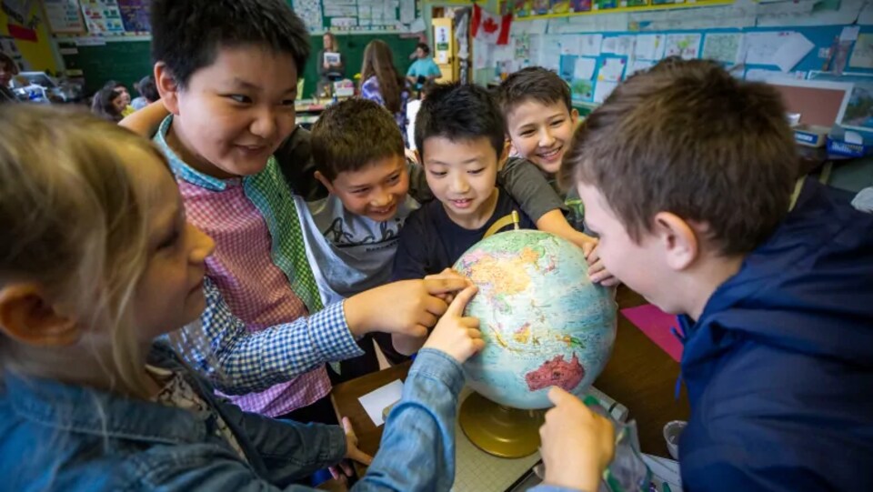 Des élèves s'amusent avec un globe terrestre dans une salle de classe. 