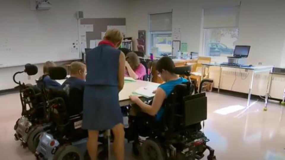 Une enseignante donne des explications à des élèves en fauteuil roulant.