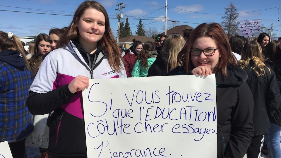 Deux adolescentes montrent une pancarte sur laquelle on peut lire : « Si vous trouvez que l'éducation coûte cher, essayez l'ignorance. »