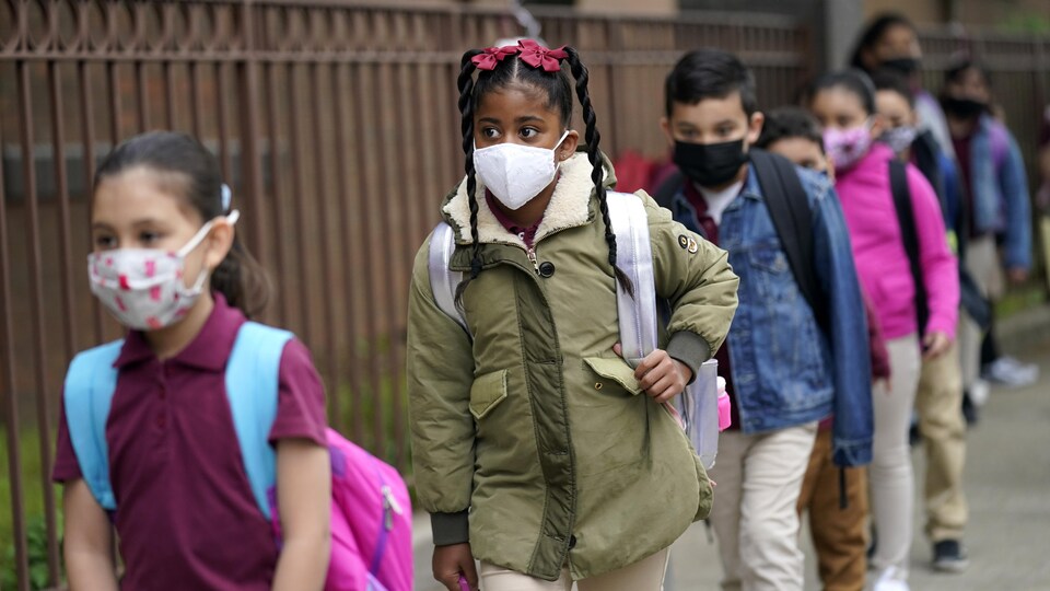 Des élèves qui portent un masque font la file pour entrer à l'école.