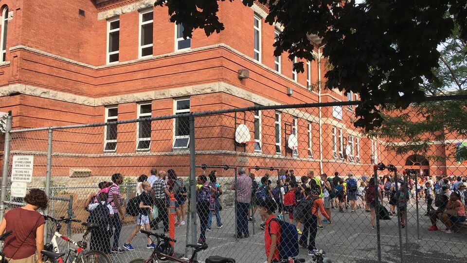 Des dizaines d'élèves sont présents dans la cour d'école.