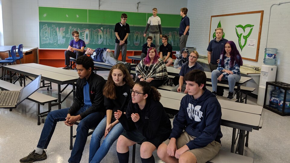 Des élèves dans une salle de classe assis et debout sur des tables.