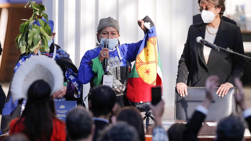 Une femme tient le drapeau mapuche en faisant un discours.
