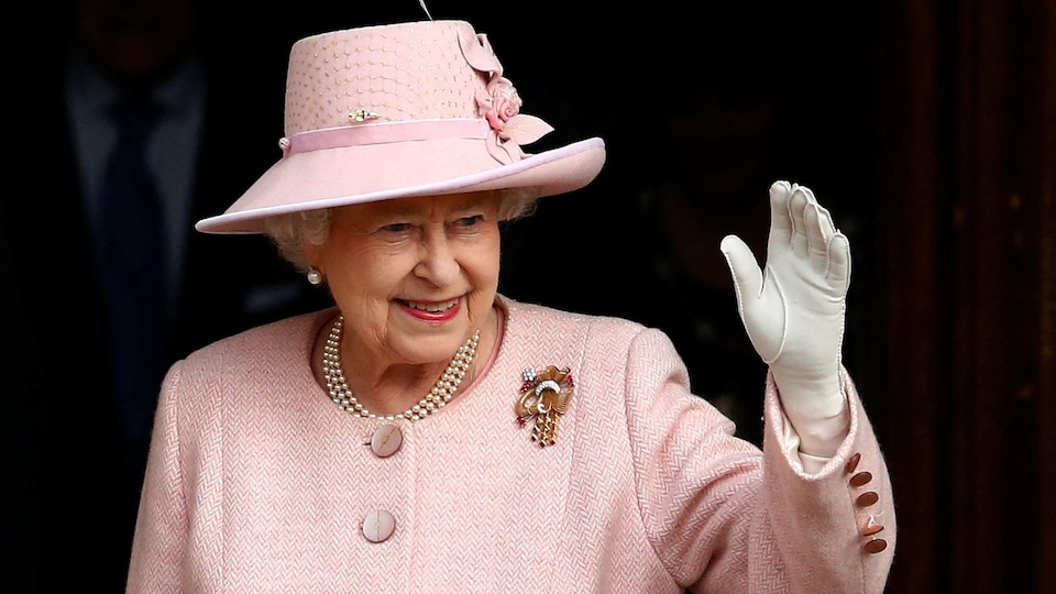 Élisabeth II, souriante, salue de sa main gantée.