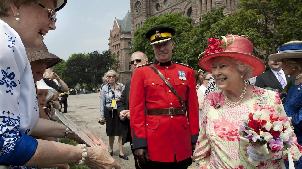 Queen Elizabeth II smiles as she presents a photo to a woman during a rally at Queen's Park in Toronto.