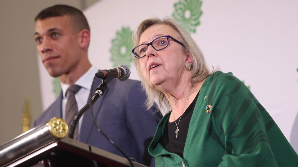 Elizabeth May et Jonathan Pedneault au pupitre devant un fond avec le logo du Parti vert canadien