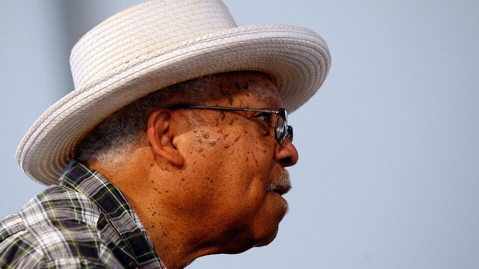 Un homme portant un chapeau blanc regarde vers la droite.