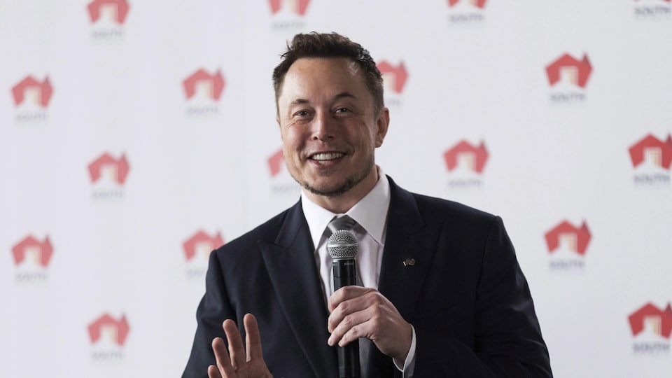 Elon Musk holding a microphone and addressing most of the off -screen.