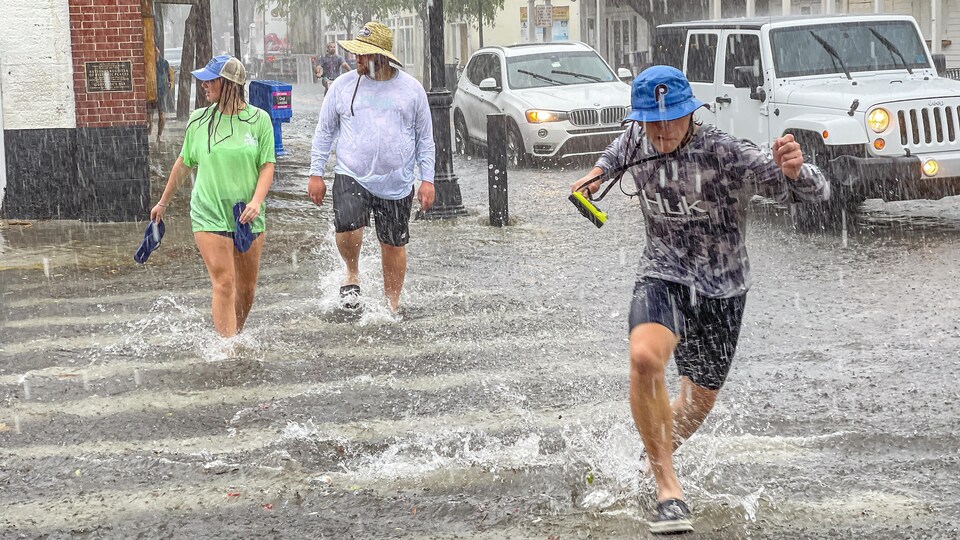 Des piétons marchent sous une pluie battante dans une rue inondée.