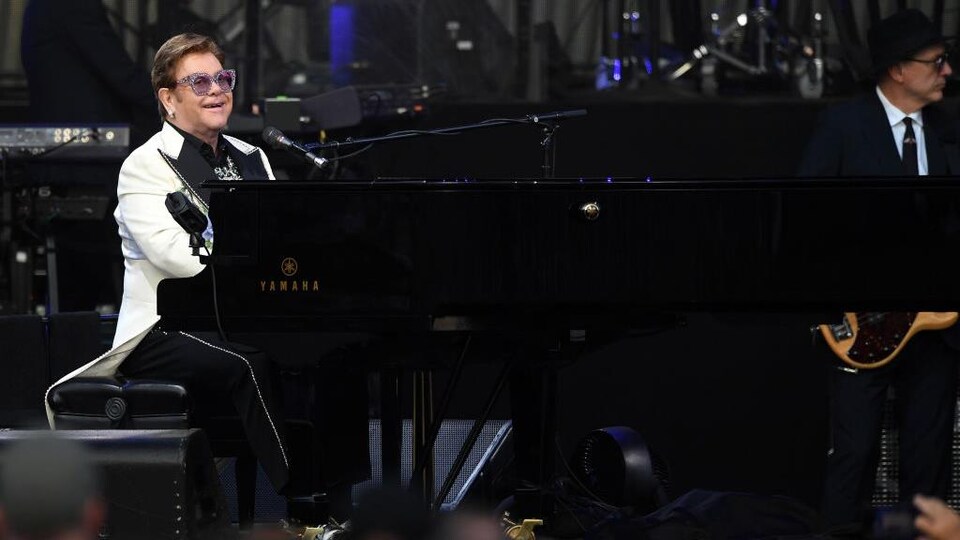 Elton John joue du piano et sourit.