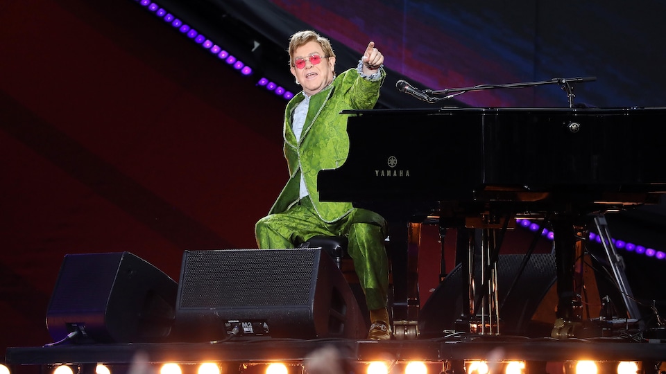 Elton John est assis derrière son piano lors d'un concert extérieur à Paris. 