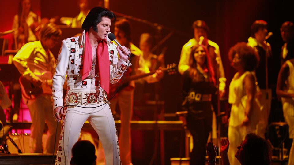 Martin Fontaine sur scène dans le rôle d'Elvis, entouré par plusieurs musiciens et choristes.