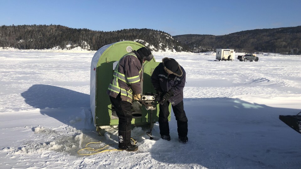 Deux pêcheurs installent une maisonnette sur la glace.