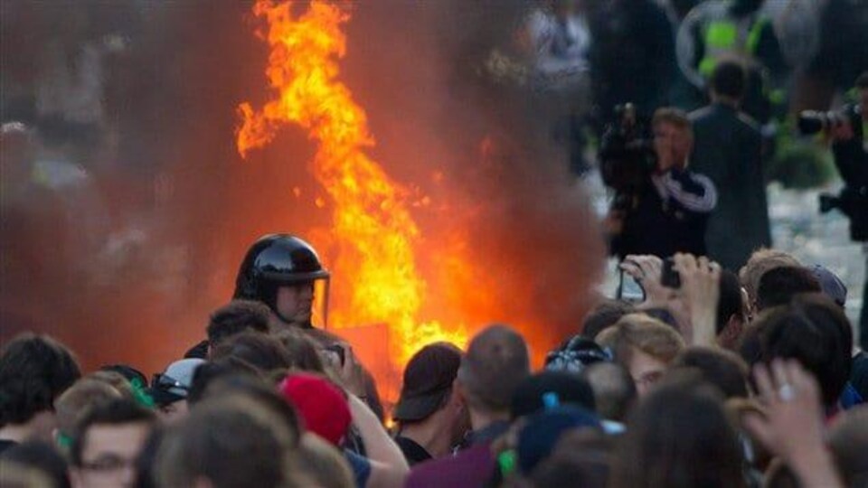 Un policier debout devant une voiture en feu est entouré d'émeutiers qui manifestent le soir de la défaite des Canucks en finale de la Coupe Stanley le 15 juin 2011.
