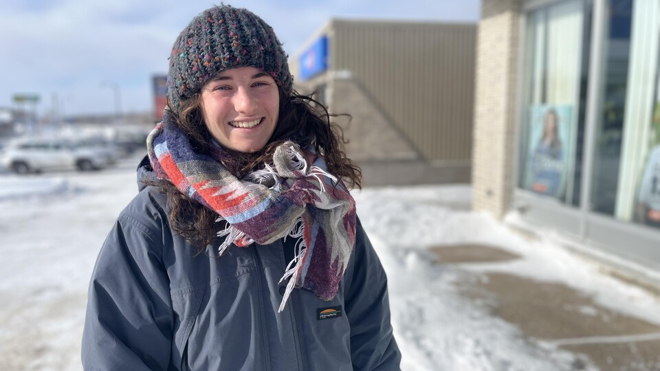 Émilie Schwartz sourit à la caméra devant le bureau de Radio-Canada à Baie-Comeau.