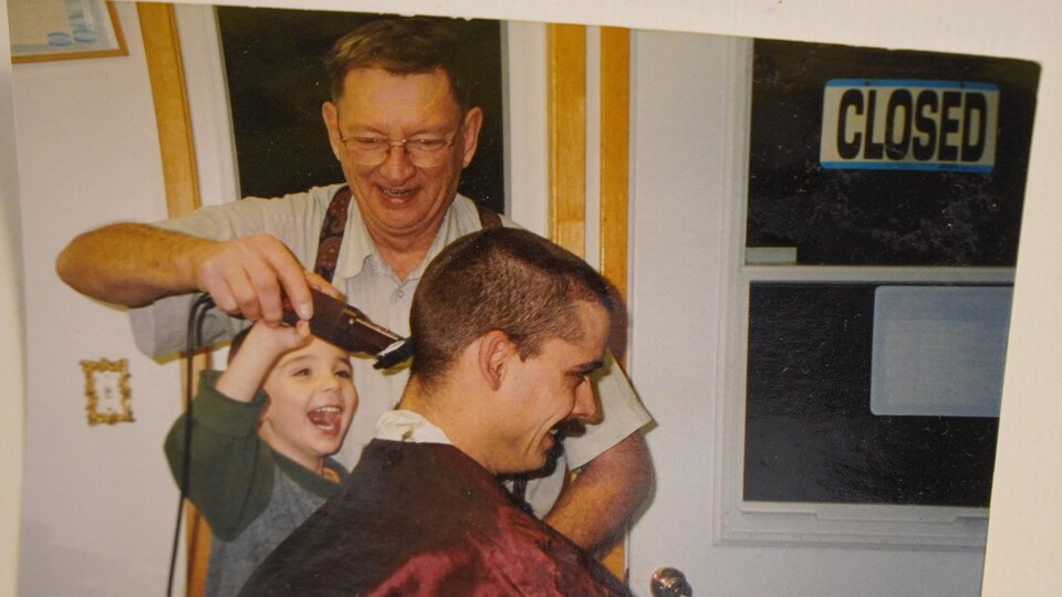 Un jeune homme coupe les cheveux de son père appuyé de son grand-père.