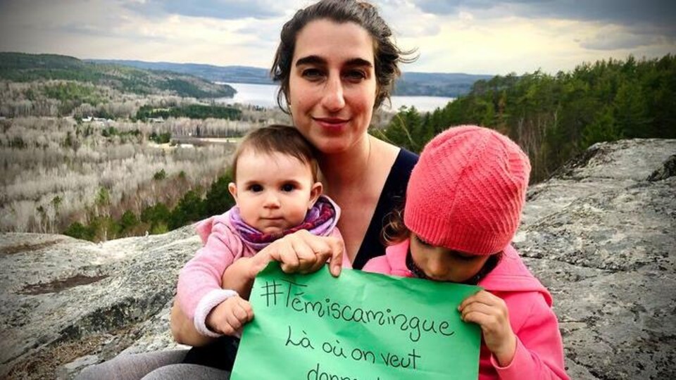 Émilise Lessard-Therrien et ses deux filles sur une colline, tenant une affiche disant «Témiscamingue, là où on veut donner la vie».
