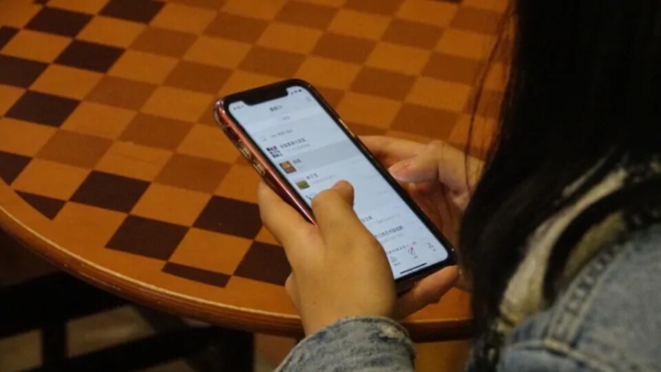 Une femme vue de dos utilise une application sur son cellulaire. 