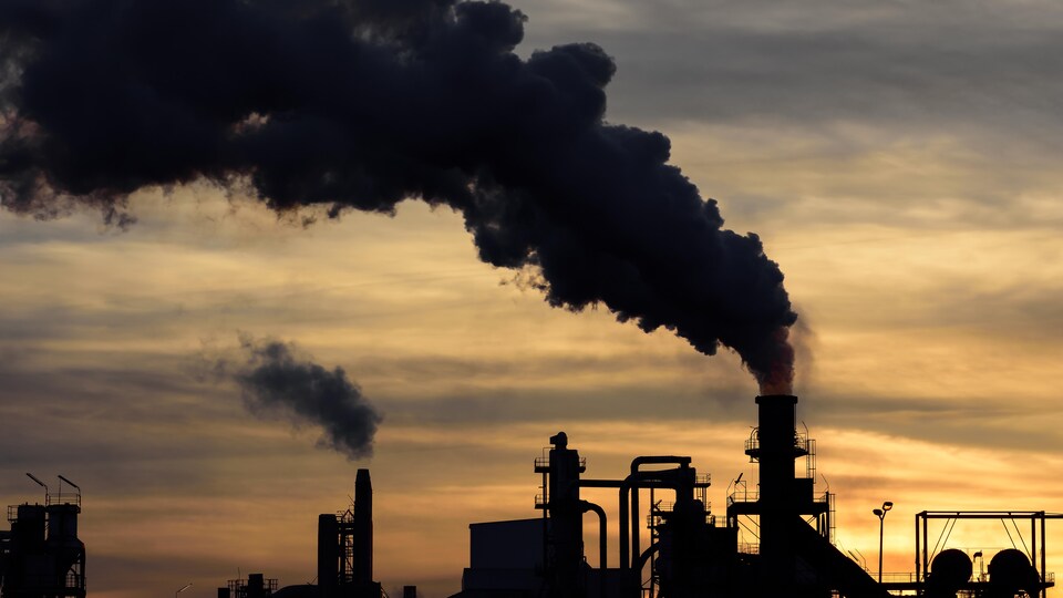 Une colonne de fumée noire s'échappe de la cheminée d'un complexe industriel.