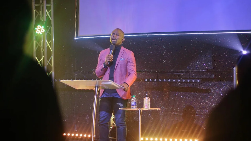 Emmanuel Adewusi est sur scène. Il a les yeux fermés et parle dans un micro.