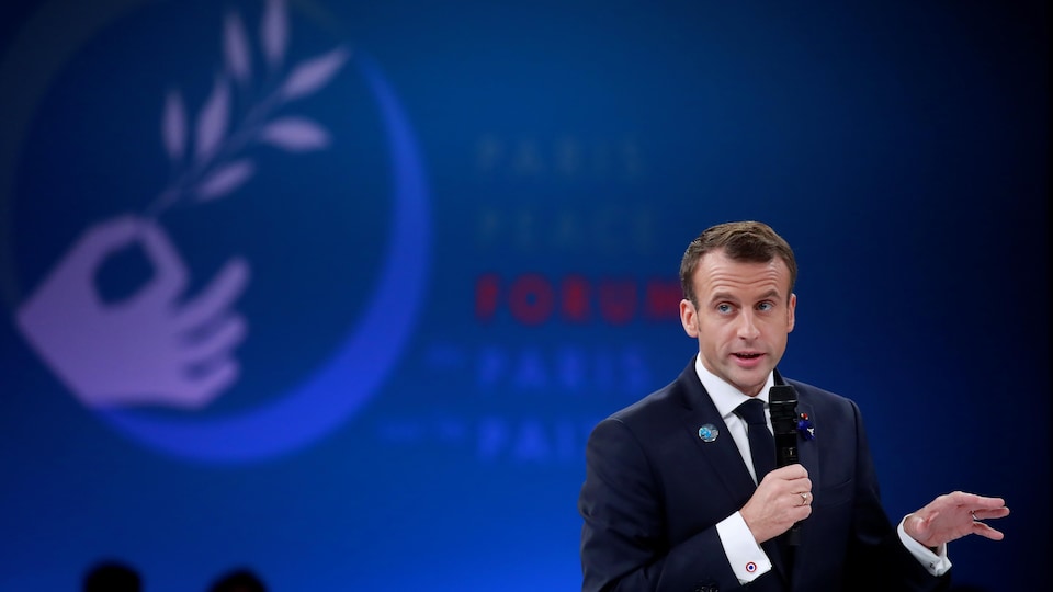 Emmanuel Macron un micro dans la main, avec derrière le dessin d'une main tenant un rameau d'olivier.