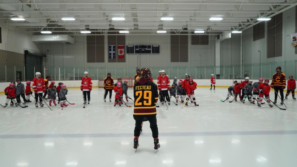 Une joueuse de dos avec devant elles plusieurs jeunes filles en équipement de hockey.