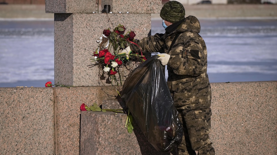 Un membre des services municipaux met dans un sac à poubelle des fleurs.