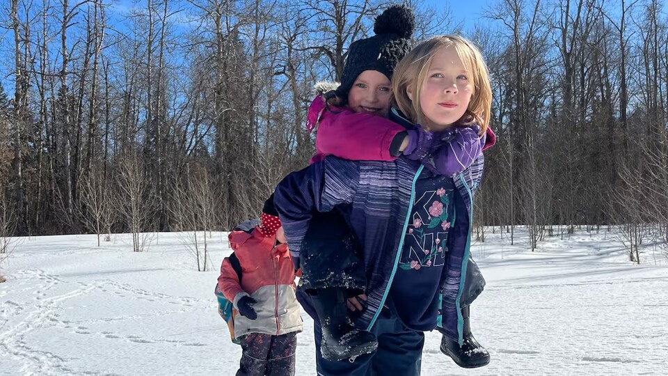 Une jeune fille de neuf ans est en raquette sur la neige en hiver et tient sur son dos un autre enfant.