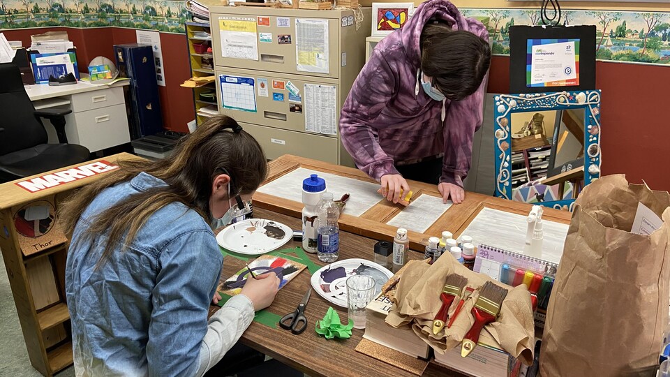 Deux jeunes femmes font de l'art, penchées sur une table.