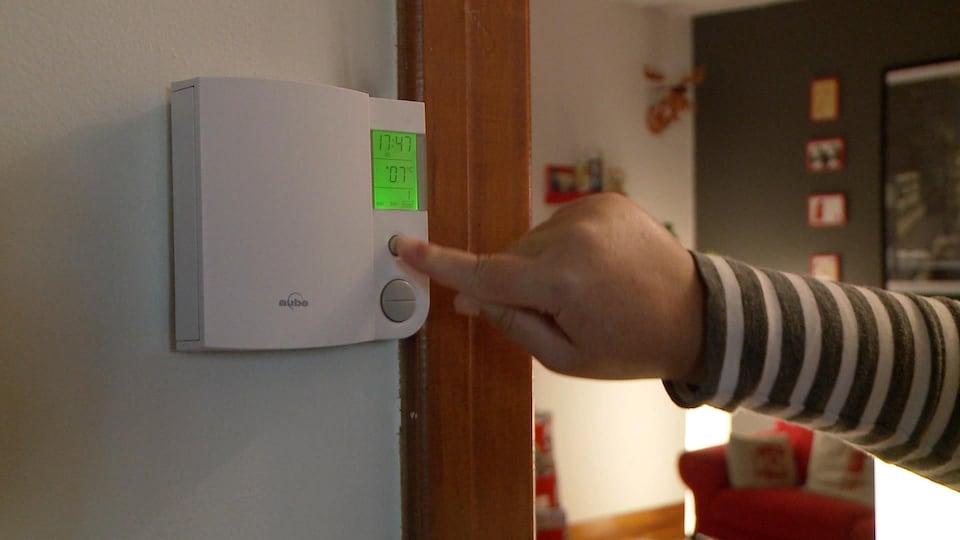 Une main appuie sur le bouton d’un thermostat électronique.