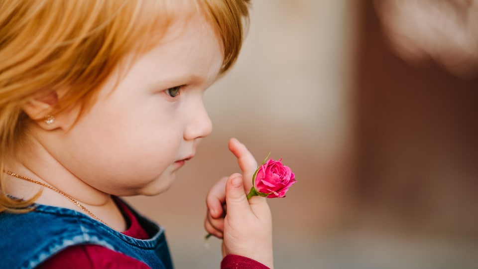 Petite fille rousse tenant une fleur dans sa main.