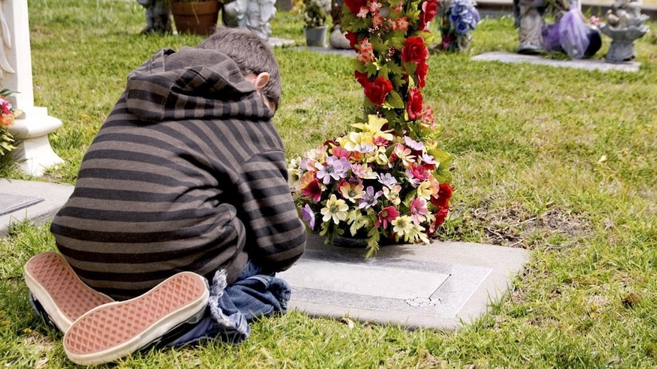 Un enfant se recueille dans un cimetière.