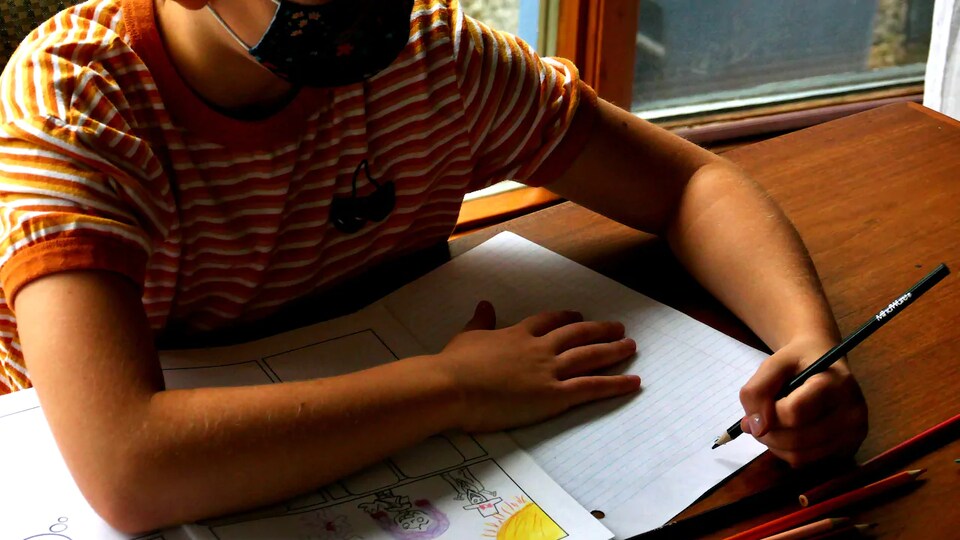 Un enfant avec un masque fait ses devoirs
