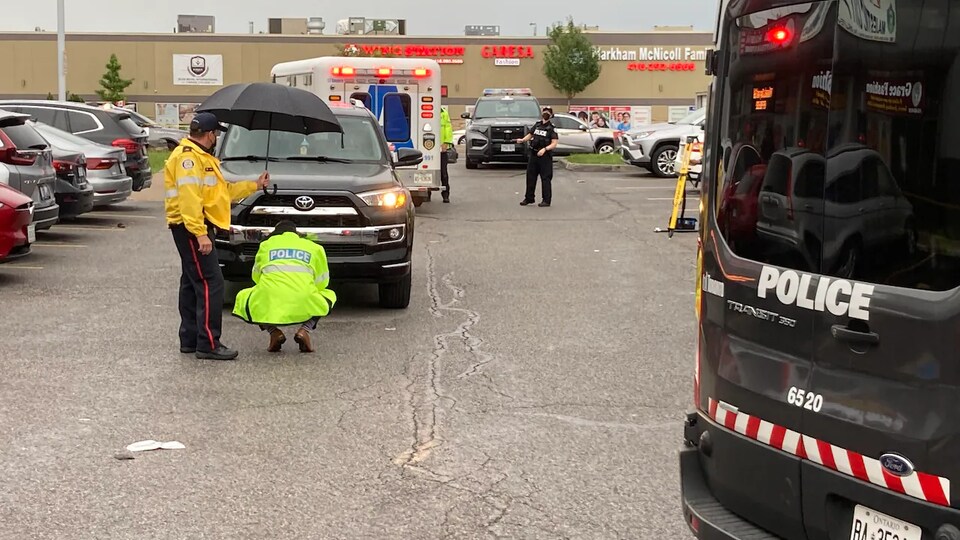 Des policiers examinent l'avant d'un véhicule après un accident mortel.