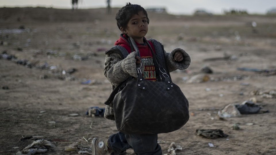 Un enfant marche seul dans une zone de guerre et porte un sac en bandoulière.