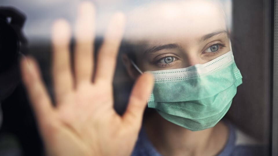 Portrait d'une adolescente portant un masque appuyée à une fenêtre.